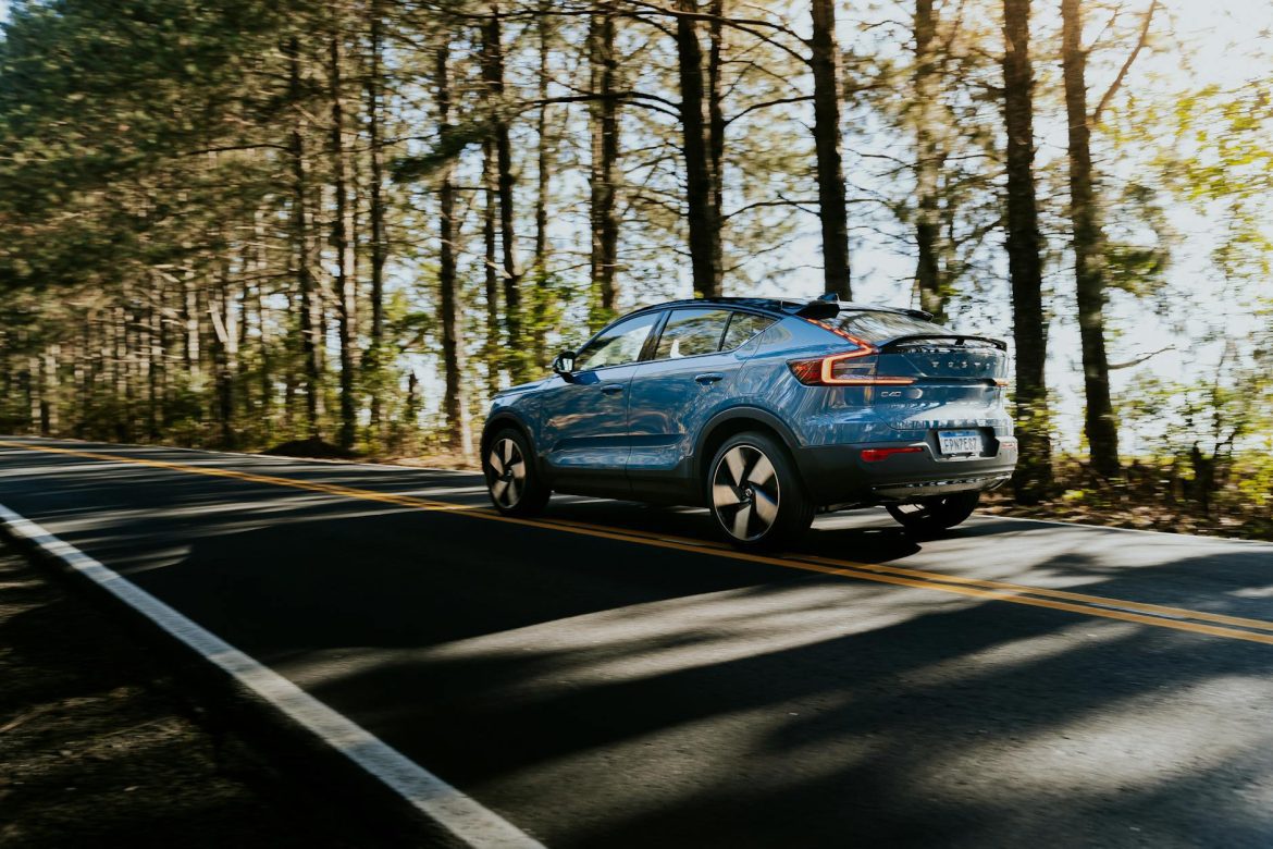 Blue electric car cruising through a scenic forest road during the day, capturing the essence of sustainable travel.