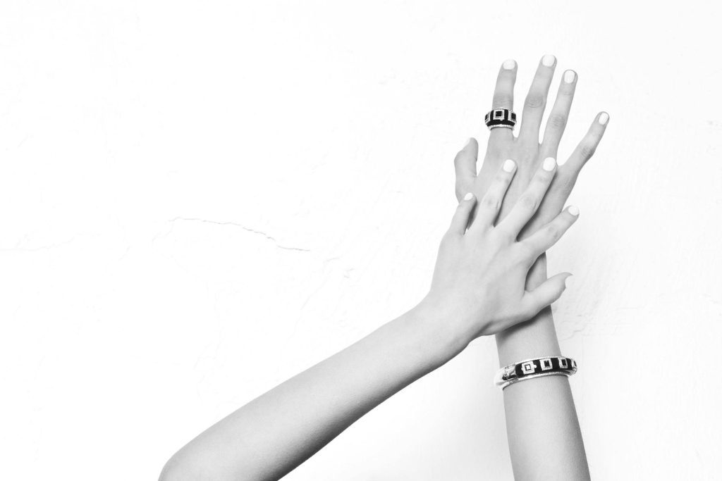 Black and white photo showcasing elegant hands adorned with rings and bracelets on a white background.