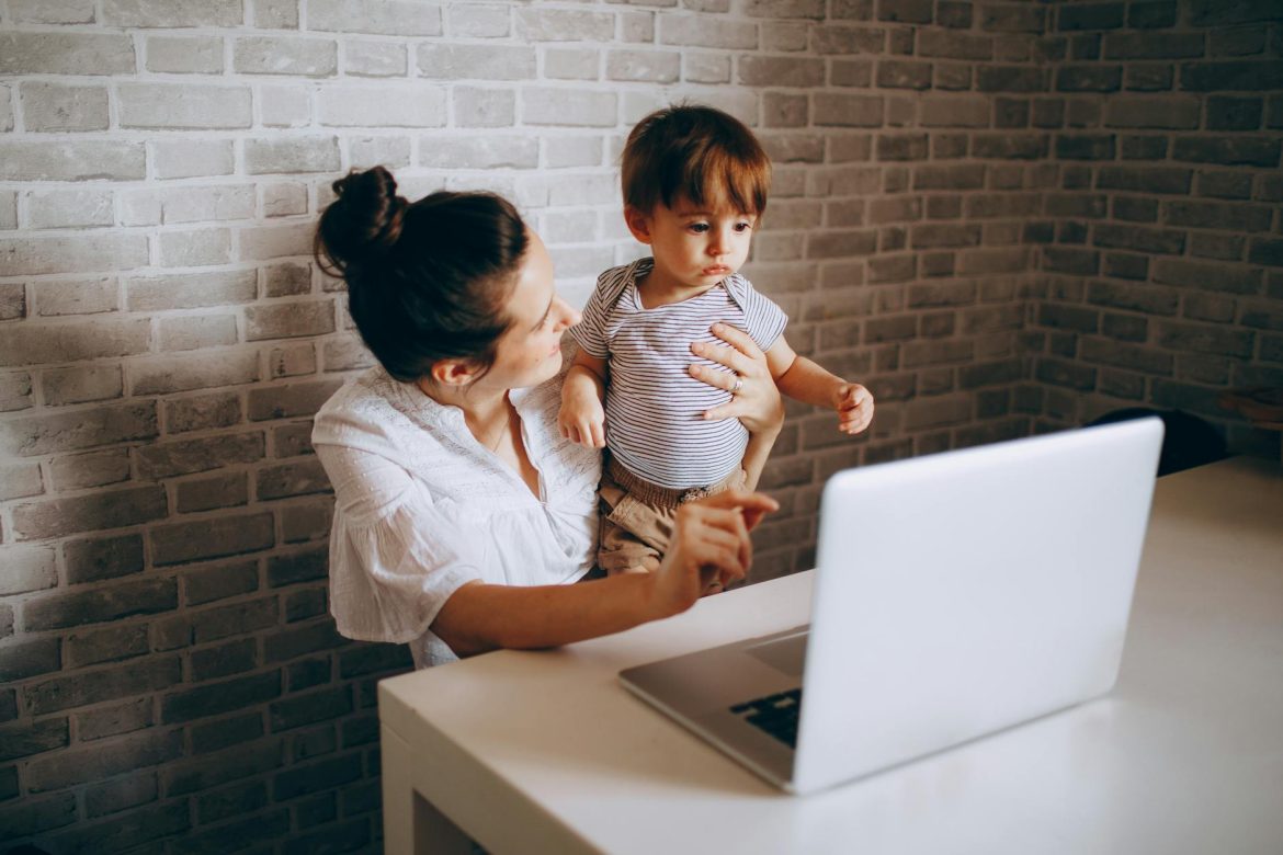 A mother holding her child while they look at a laptop together indoors.